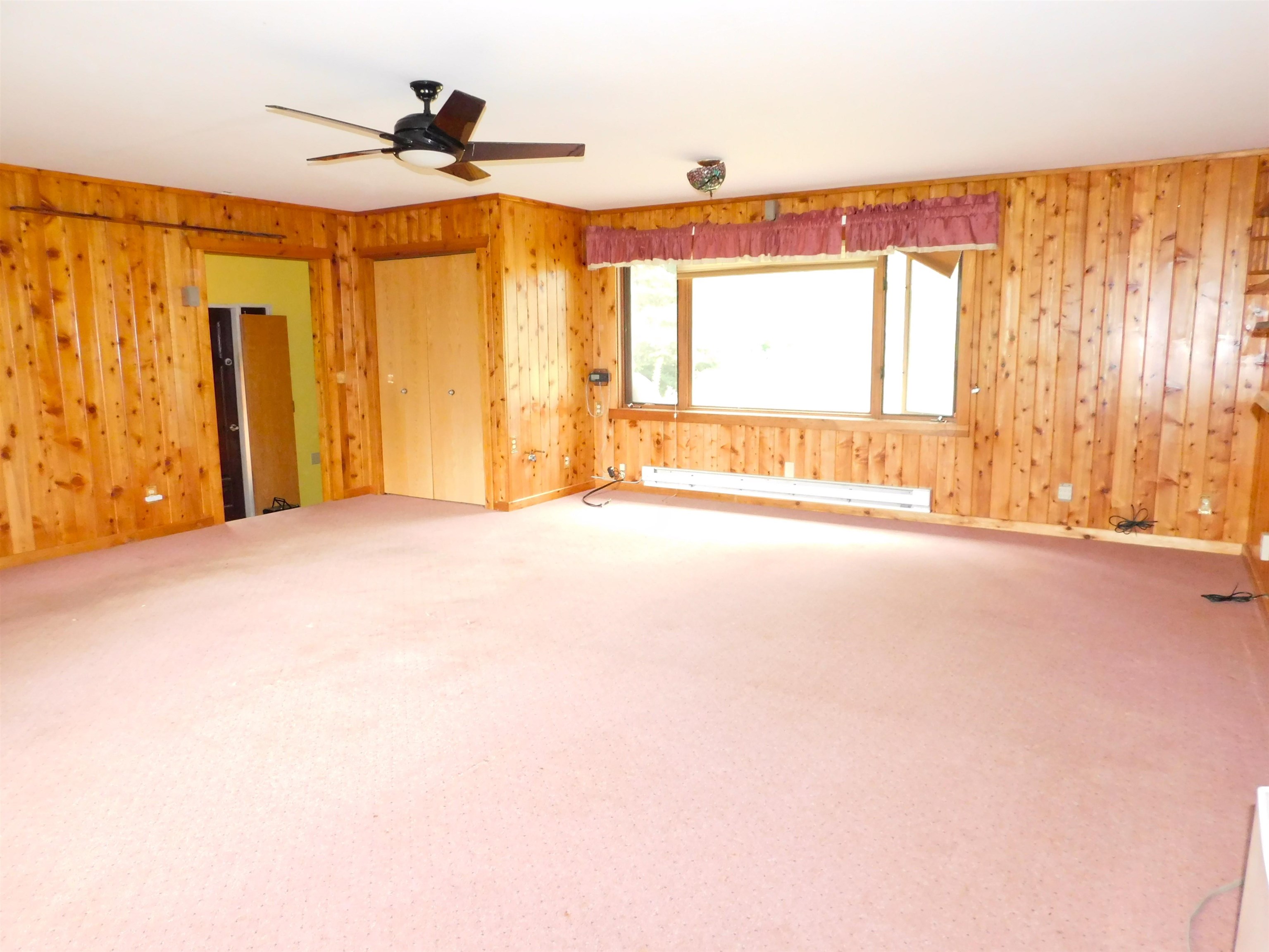4036 County Rd A Superior, WI 54880 - Photo 11 of 52 Unfurnished room featuring wooden walls, carpet floors, a baseboard radiator, and a ceiling fan