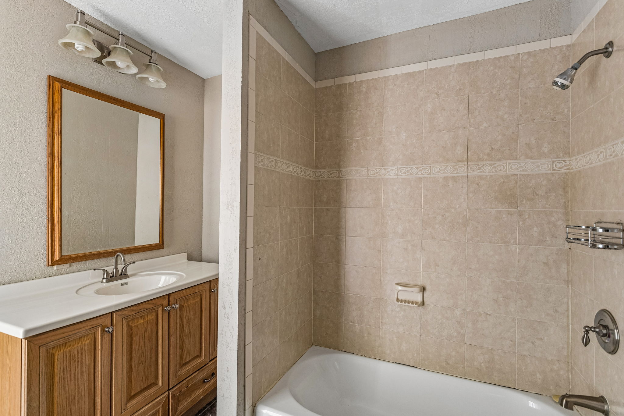 9765 A State Park Road Lockhart, TX 78644 - Photo 14 of 30 A well-maintained bath area boasts a built-in tub with neutral tiled walls, complemented by a vanity with a white countertop and framed mirror.