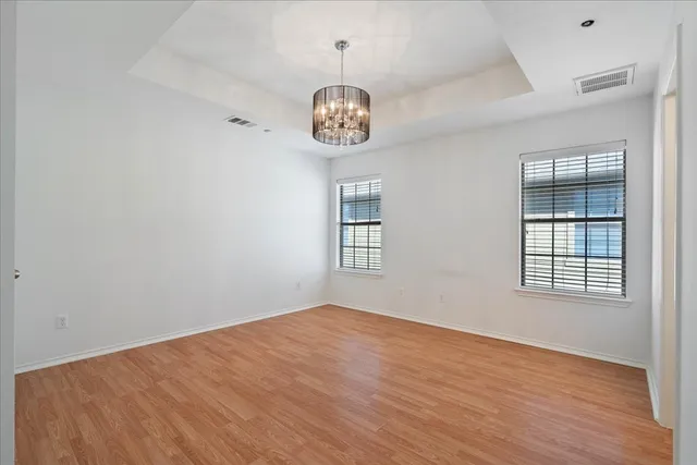 an empty room with wooden floor chandelier fan and windows