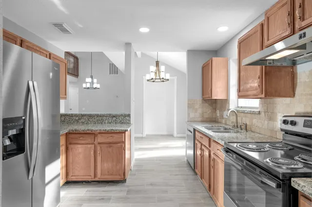 a kitchen with stainless steel appliances granite countertop a refrigerator a stove and a sink with wooden floors