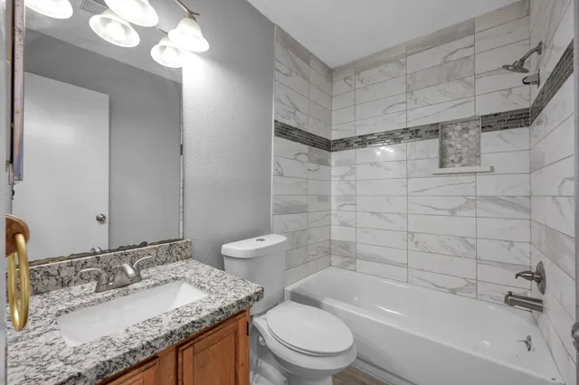 a bathroom with a granite countertop sink a toilet and bathtub