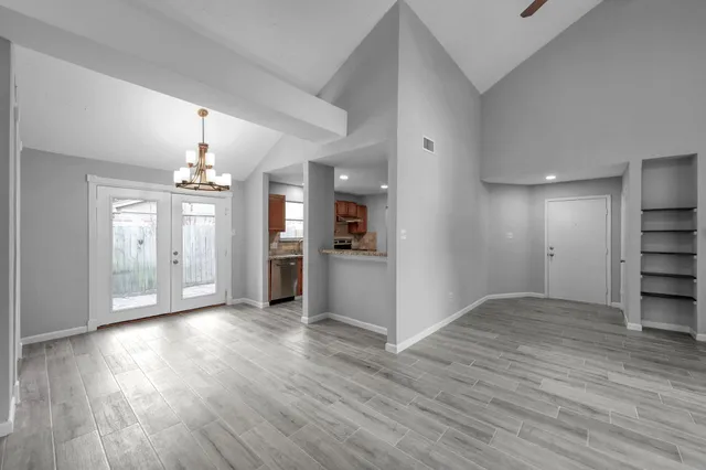 an empty room with wooden floor chandelier and windows