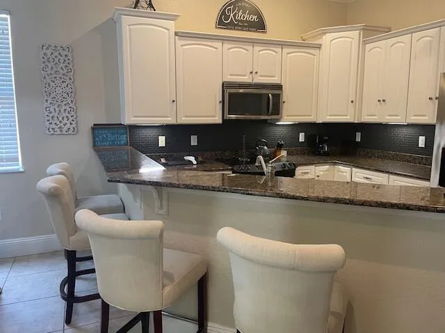 a kitchen with stainless steel appliances granite countertop a sink a stove a microwave a dining table and chairs with white cabinets