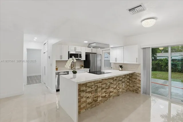 a large kitchen with kitchen island a large counter top stainless steel appliances and cabinets