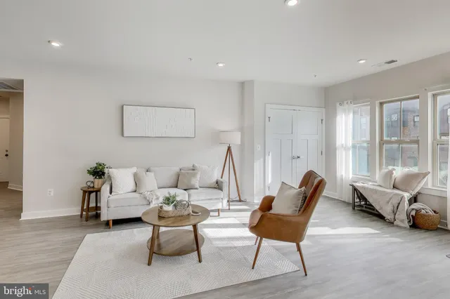 a living room with lots of furniture kitchen view and a large window