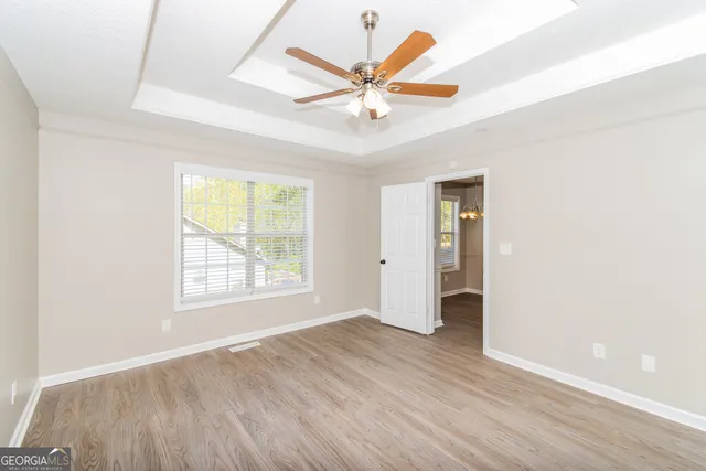 an empty room with wooden floor ceiling fan and windows