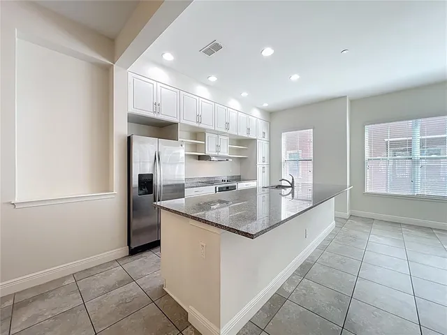 a kitchen with stainless steel appliances granite countertop a sink dishwasher a refrigerator and white cabinets with wooden floor