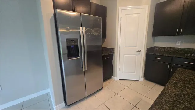 a view of a refrigerator in kitchen and an empty room in wooden floor