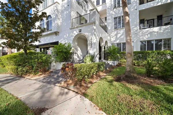 a front view of a multi story residential apartment building with yard and parking