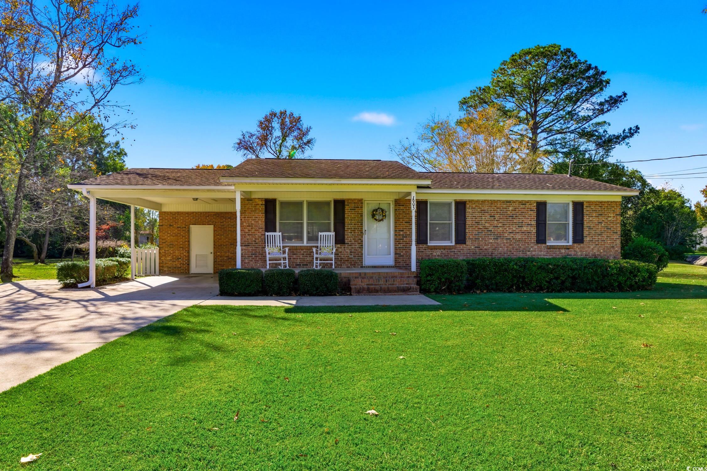 Ranch-style home featuring a porch, a front yard, concrete driveway, and an attached carport