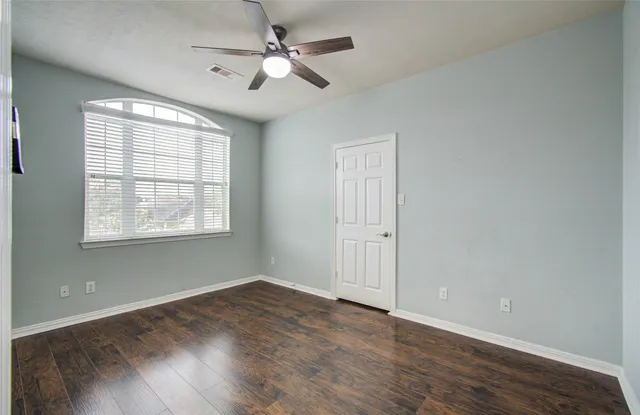 an empty room with wooden floor ceiling fan and windows