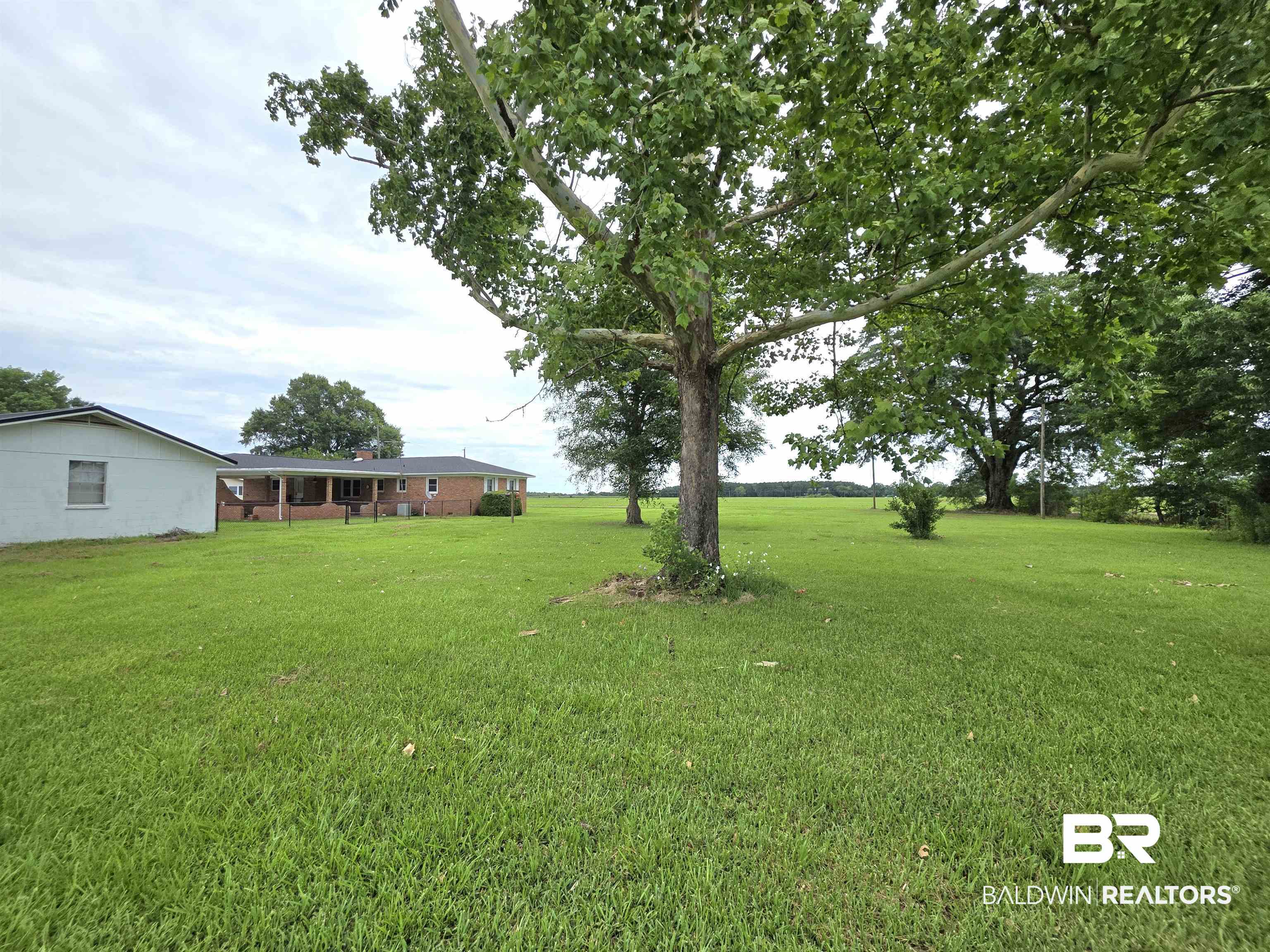 558 Stanton Road Atmore, AL 36502 - Photo 24 of 29 Expansive green lawn with mature trees and a distant brick residence featuring a covered back patio