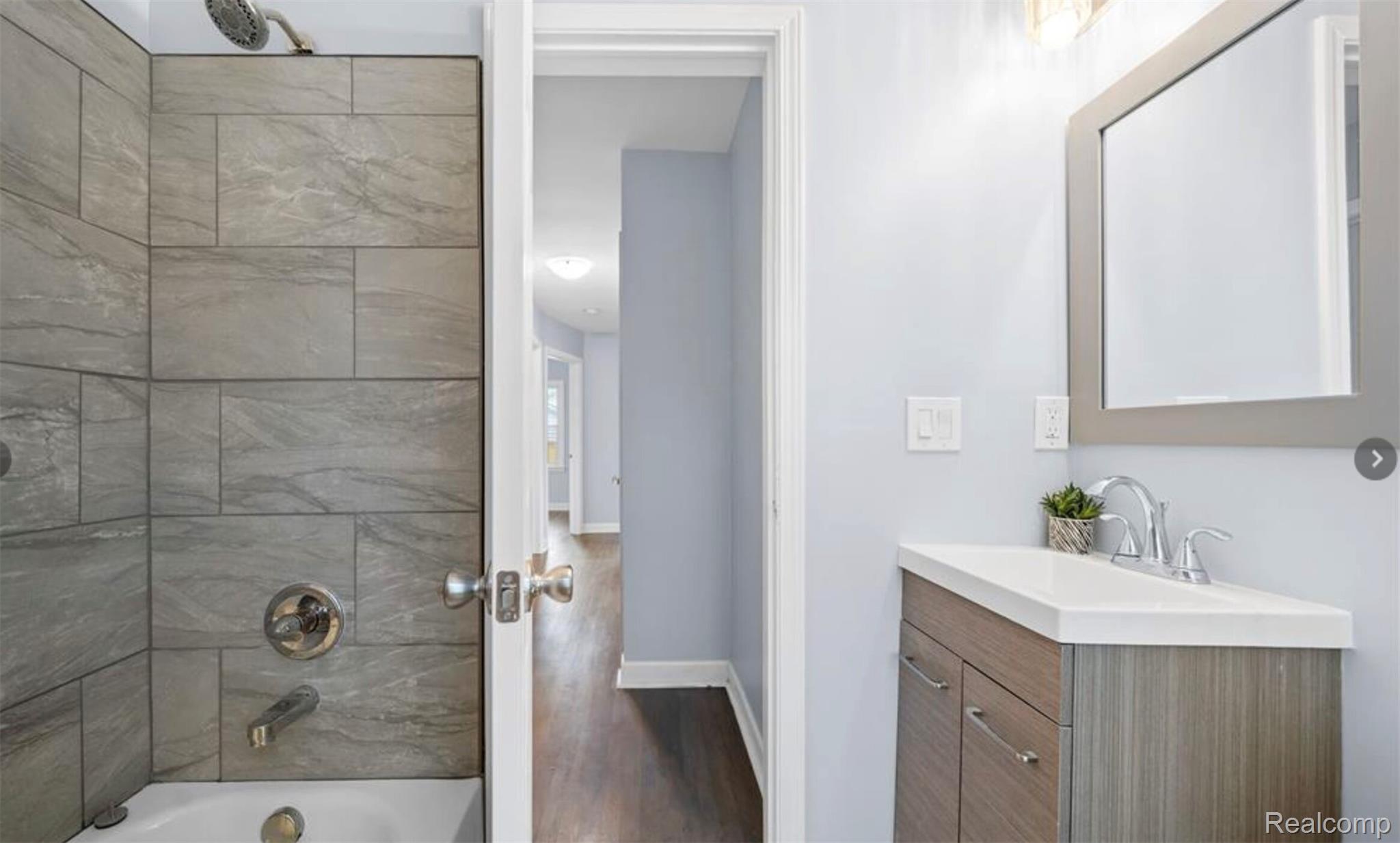 4214 Berkshire Road Royal Oak, MI 48073 - Photo 19 of 27 Contemporary bathroom featuring a wood-finish vanity with a white countertop and chrome faucet, a rectangular mirror, and a shower with gray tile surround and chrome fixtures