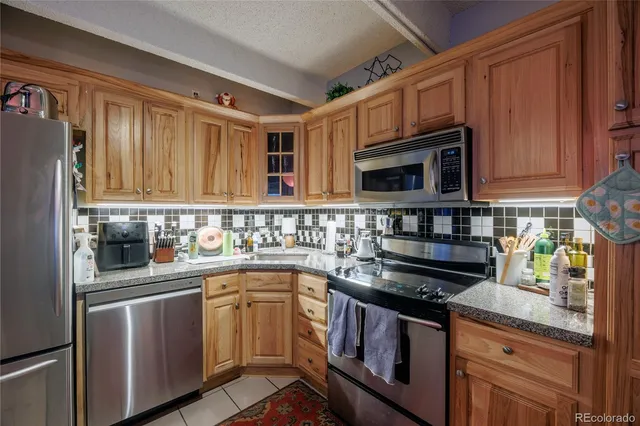 a kitchen with stainless steel appliances granite countertop a stove top oven a sink dishwasher and a refrigerator with wooden cabinets