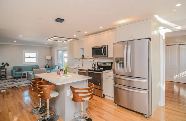 a kitchen with a refrigerator a stove a microwave oven a sink with island and chairs with wooden floor