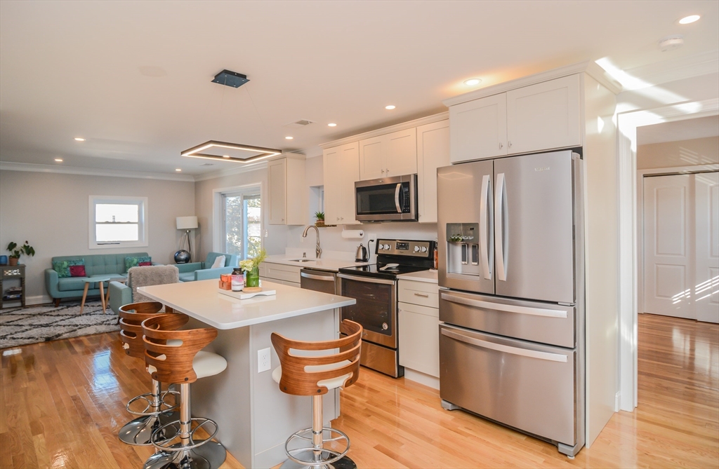 a kitchen with a refrigerator a stove a microwave oven a sink with island and chairs with wooden floor