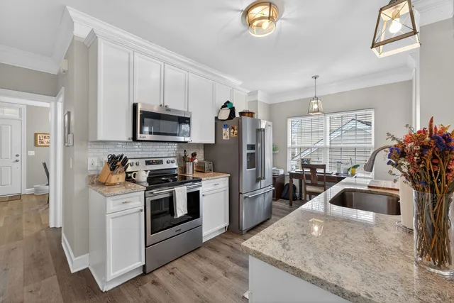 a kitchen with stainless steel appliances granite countertop a sink a stove a refrigerator a microwave a dining table and chairs with wooden floor