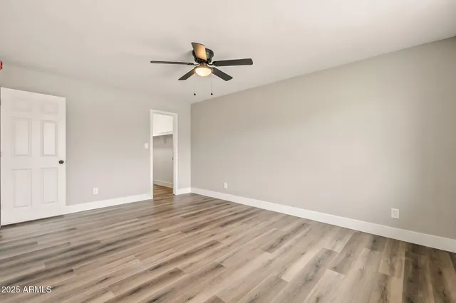 a view of an empty room with wooden floor and a ceiling fan