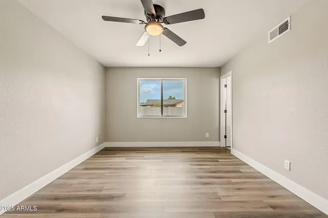 an empty room with wooden floor ceiling fan and windows
