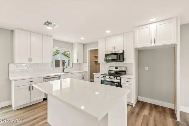 a large white kitchen with wooden floor a sink and stainless steel appliances