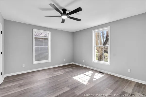 an empty room with wooden floor windows and fan