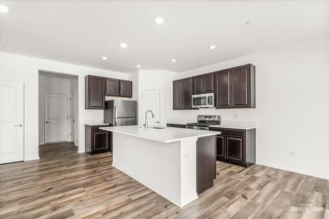 a kitchen with stainless steel appliances a stove top oven a sink a refrigerator white cabinets and wooden floor