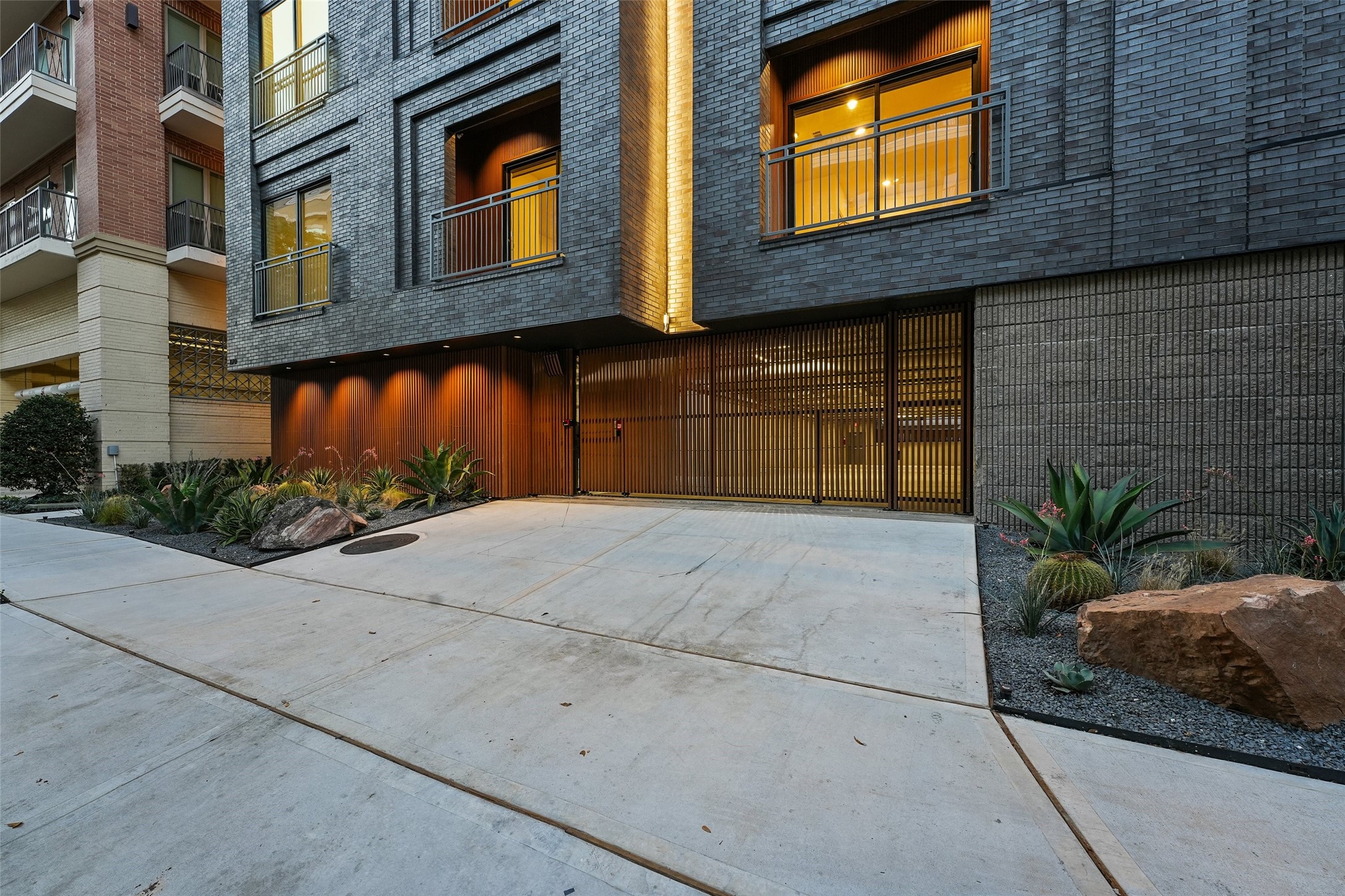 170 Malone Street, Unit 3401 Houston, TX 77007 - Photo 12 of 28 This modern apartment building features an elegant exterior with dark brickwork, warm lighting, and stylish metal accents. The entrance is framed by contemporary landscaping, including rocks and succulents, offering a welcoming and upscale appearance.