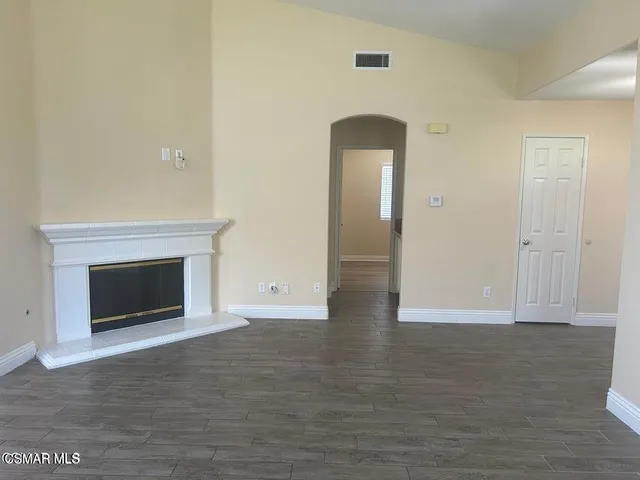an empty room with wooden floor fireplace and hallway