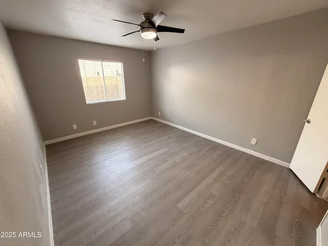 an empty room with wooden floor fan and windows