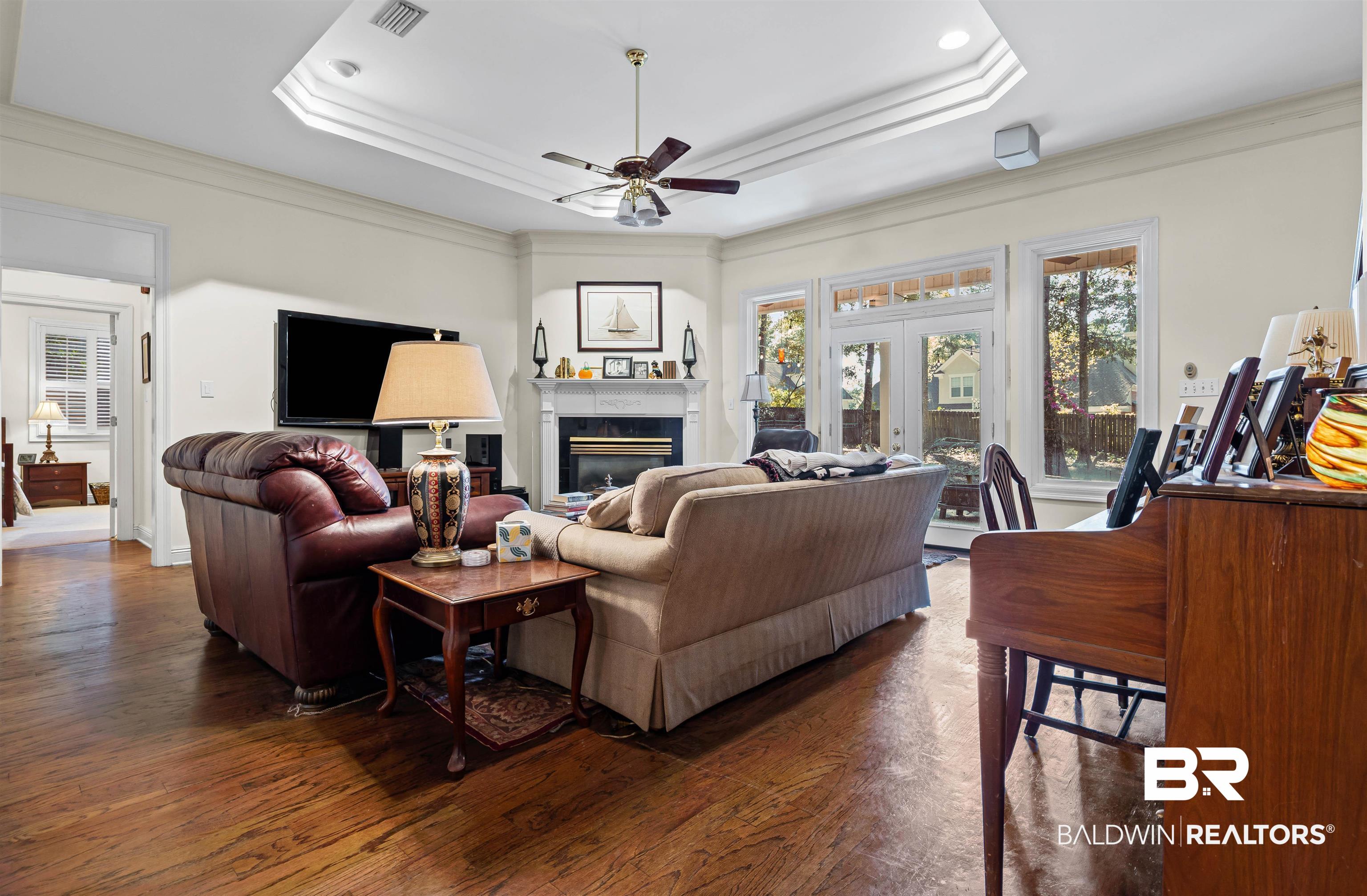 107 Beaver Dam Road Fairhope, AL 36532 - Photo 2 of 45 Living area with a raised ceiling, a glass covered fireplace, dark wood finished floors, ornamental molding, and a ceiling fan