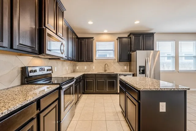 a kitchen with stainless steel appliances granite countertop a stove top oven a sink dishwasher a refrigerator and a cabinets with wooden floor