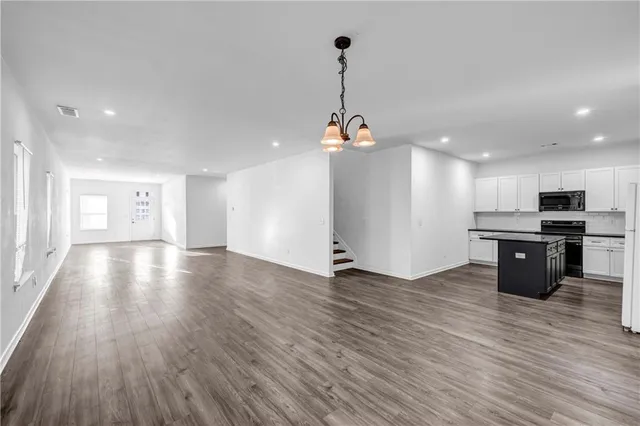 an empty room with wooden floor and kitchen view