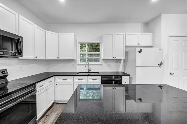 a kitchen with granite countertop a refrigerator stove and white cabinets