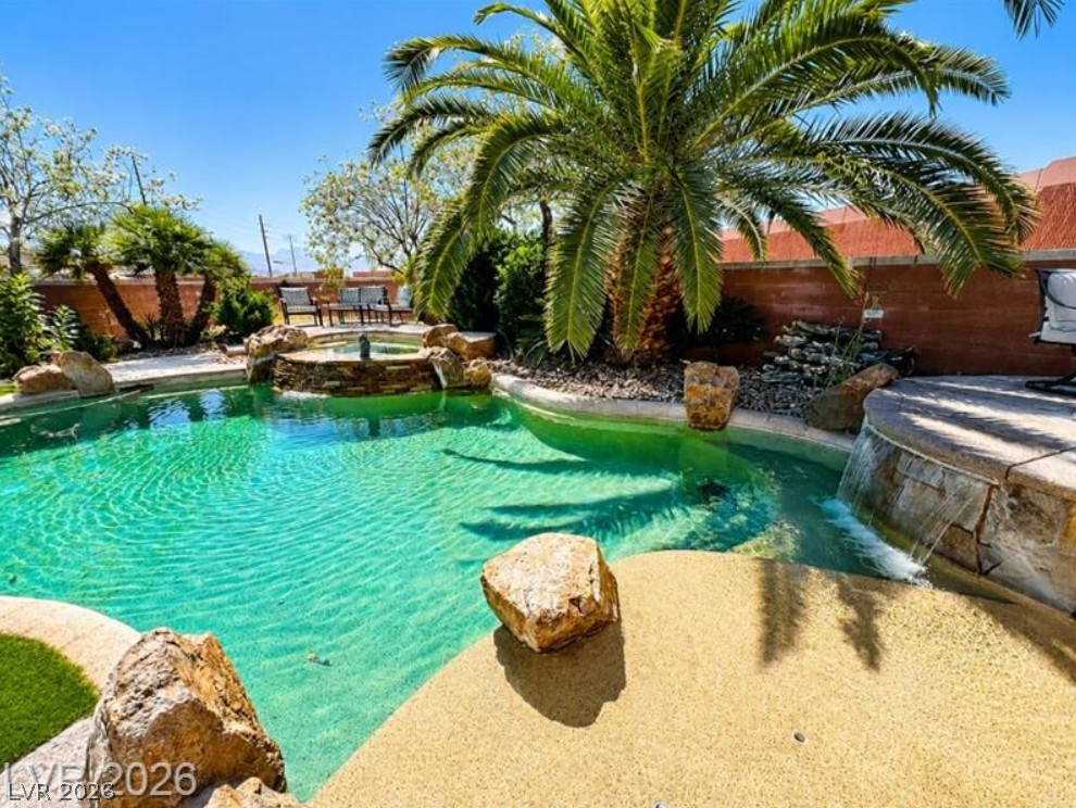 6405 North Raptor Court North Las Vegas, NV 89084 - Photo 41 of 66 A tranquil oasis awaits, featuring a freeform swimming pool with a stone waterfall and lush palm trees.