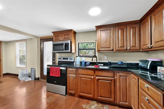 a kitchen with stainless steel appliances granite countertop a stove top oven a sink dishwasher a dining table and chairs with wooden floor