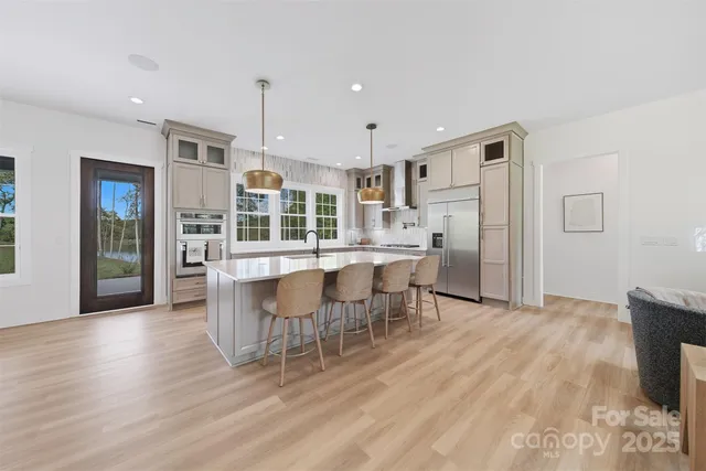 a kitchen with stainless steel appliances kitchen island granite countertop a refrigerator a stove top oven and a dining table with wooden floor