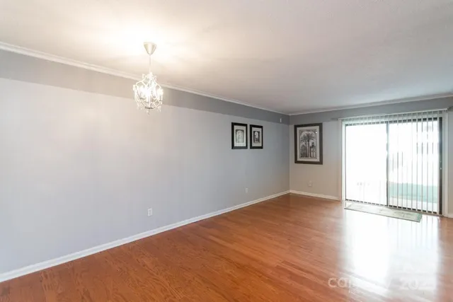 an empty room with wooden floor chandelier and windows