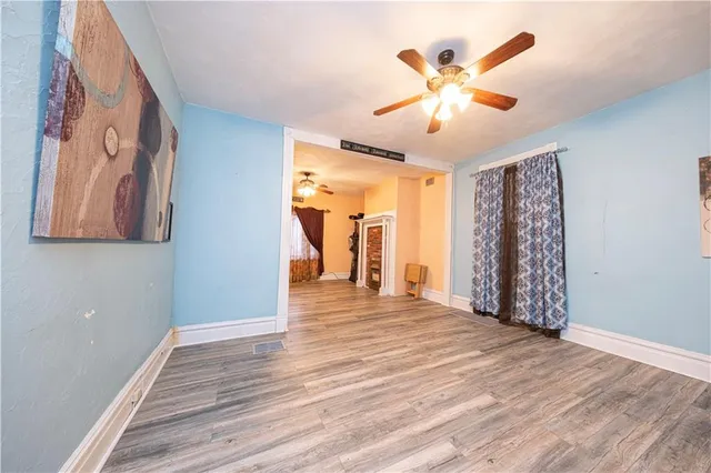 a view of an empty room with wooden floor and a ceiling fan