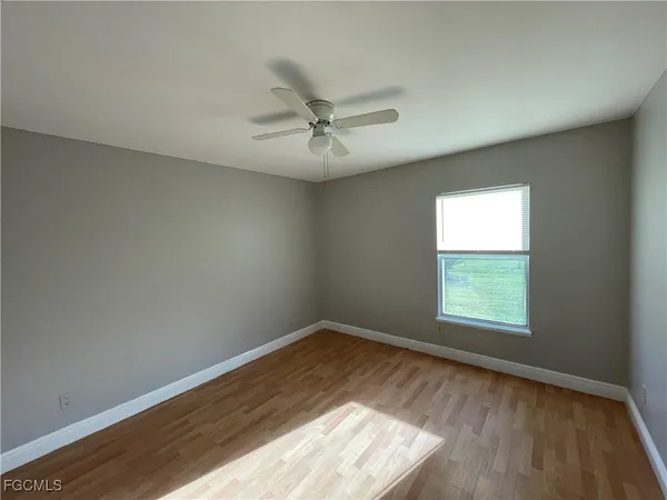 an empty room with wooden floor ceiling fan and windows