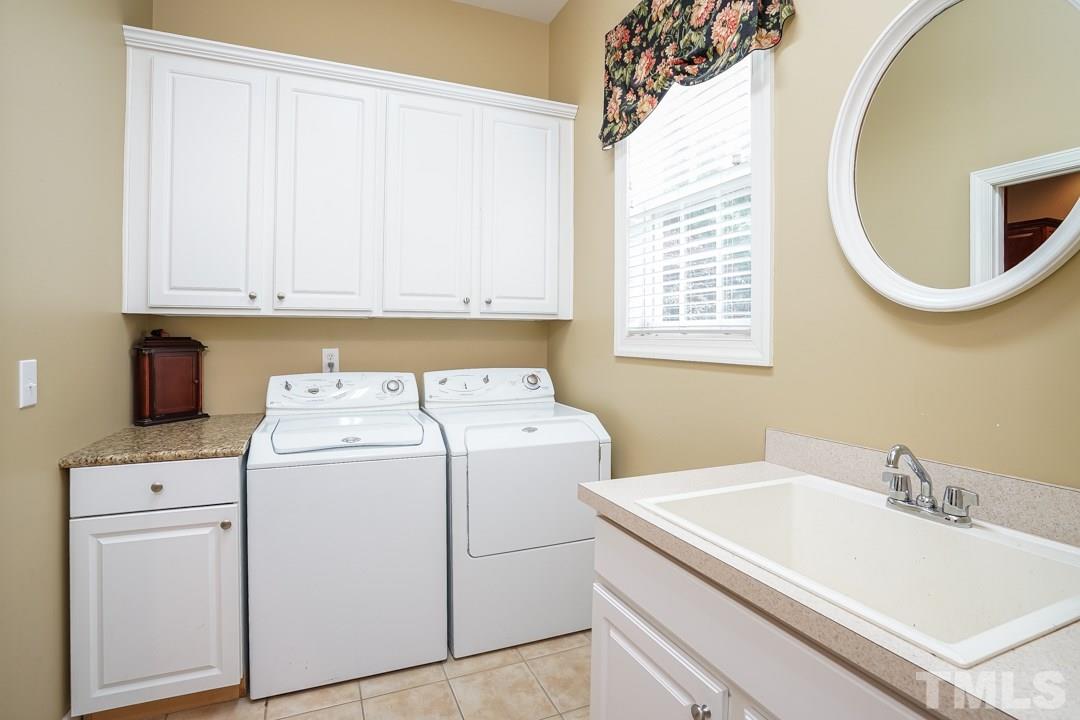 2920 Elmfield Street Raleigh, NC 27614 - Photo 14 of 30 The laundry connects the two car garage to the kitchen. Cabinetry for storage, a utility sink, tile floors and a coat closet.