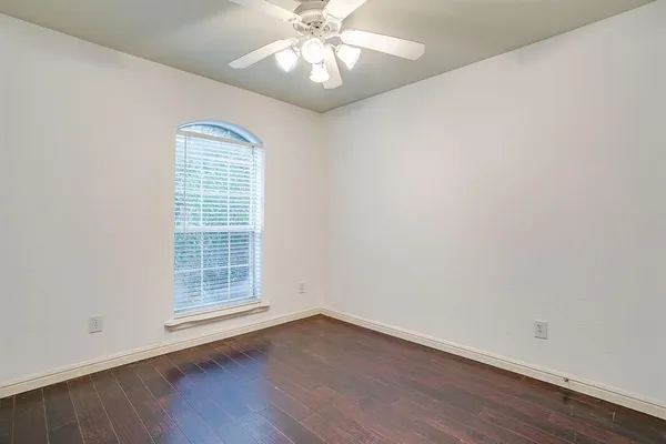an empty room with wooden floor fan and windows