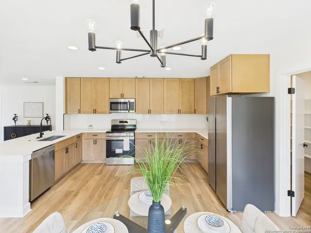 a kitchen with stainless steel appliances granite countertop a refrigerator a stove a sink dishwasher and a dining table with wooden floor