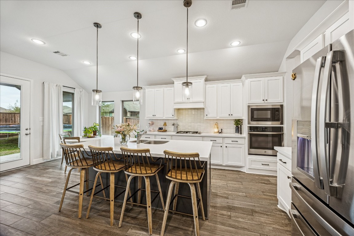4527 Peloton Road Rosharon, TX 77583 - Photo 13 of 30 a kitchen with stainless steel appliances granite countertop a stove top oven a refrigerator a kitchen island a dining table and chairs with wooden floor