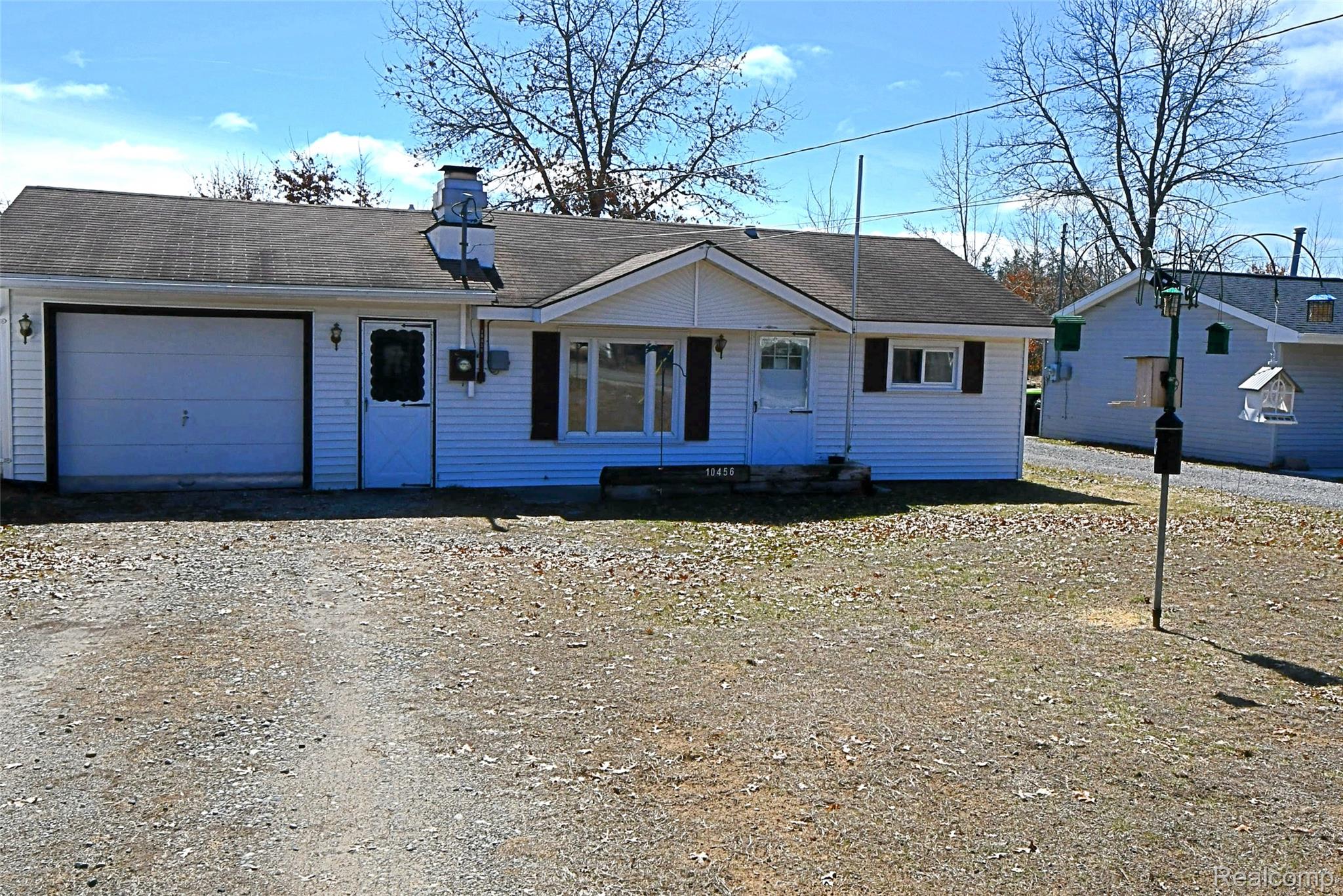 10456 Austin Road St. Helen, MI 48656 - Photo 5 of 24 View of front of property featuring an attached garage, dirt driveway, a chimney, and roof with shingles