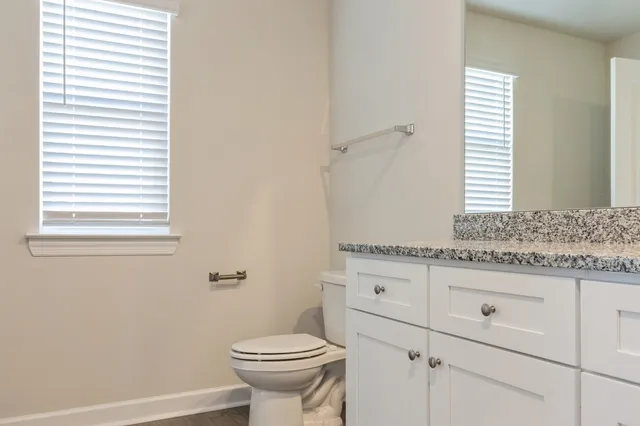 a bathroom with a granite countertop sink a toilet and a window