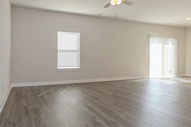 an empty room with wooden floor chandelier fan and windows