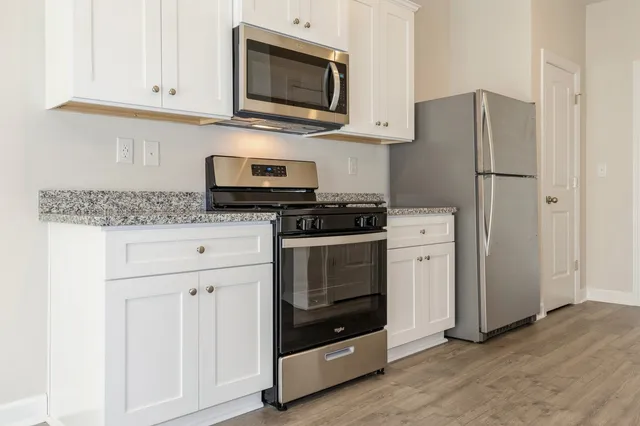a kitchen with stainless steel appliances granite countertop white cabinets a refrigerator and a stove top oven