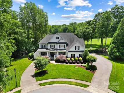 a view of a white house with a big yard plants and large trees