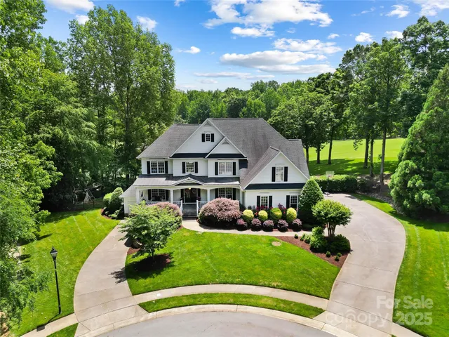 a view of a white house with a big yard plants and large trees
