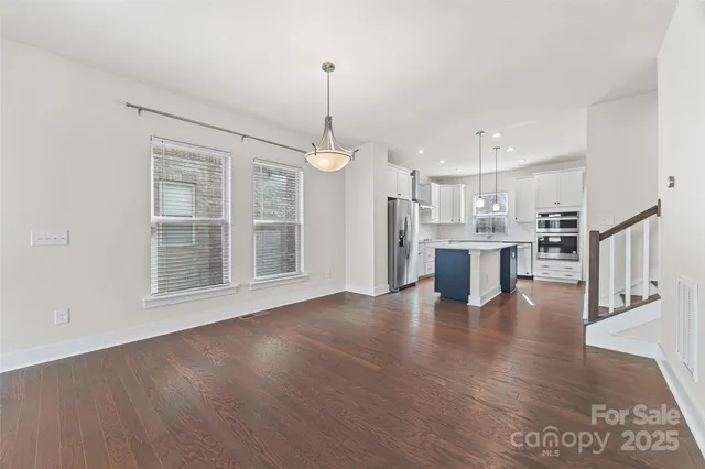 a view of an empty room with wooden floor kitchen view and a window